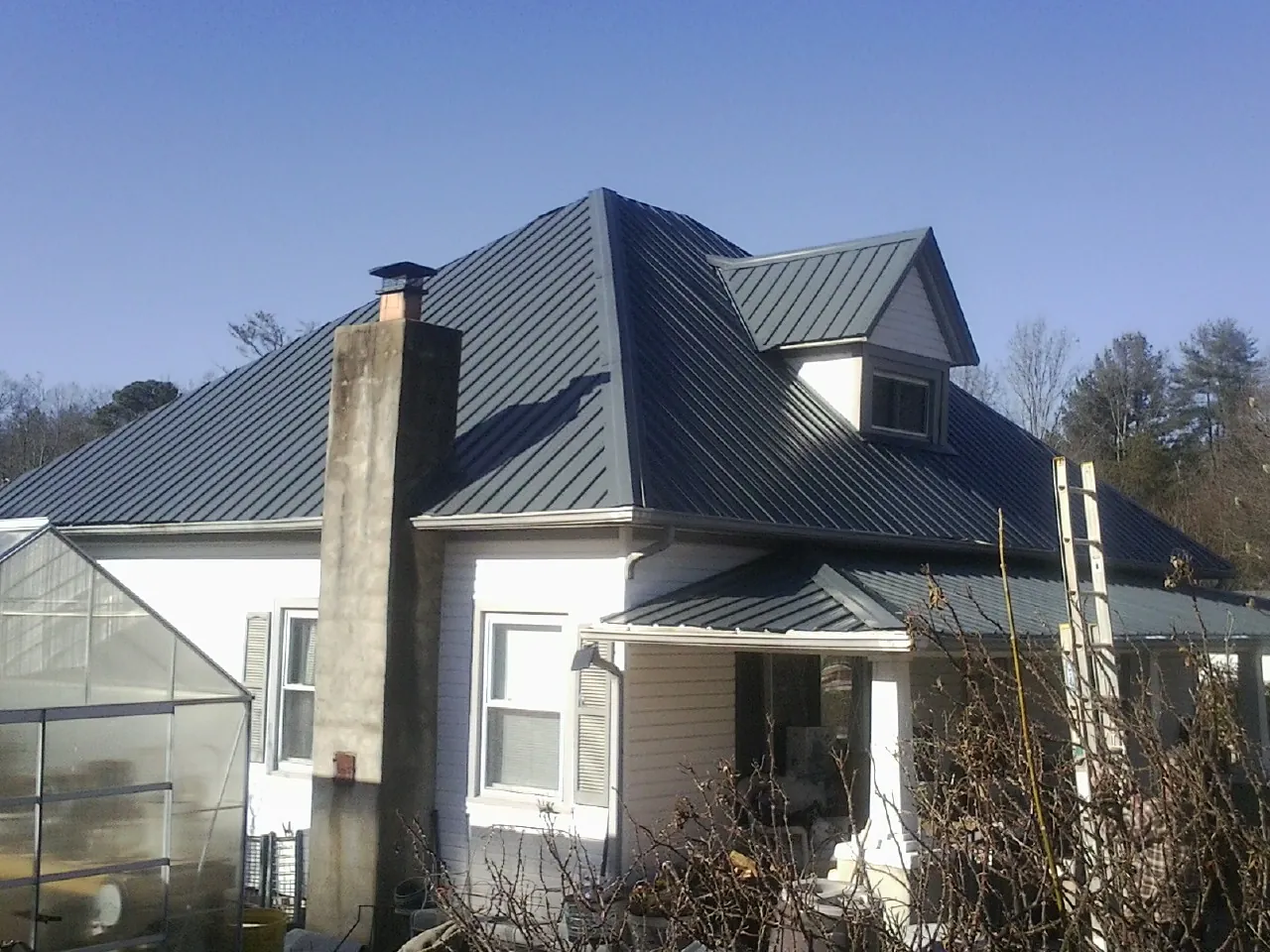 Dark blue standing seam metal roof on a white farmhouse with dormer — Slate & Tile Roof Repair by Roofing Brothers in Nodaway