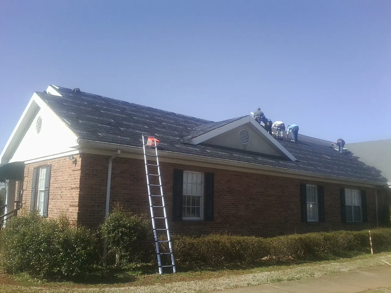 Crew tearing shingles off a brick ranch roof with a ladder set — Emergency Roof Repair work by our crew in Nodaway