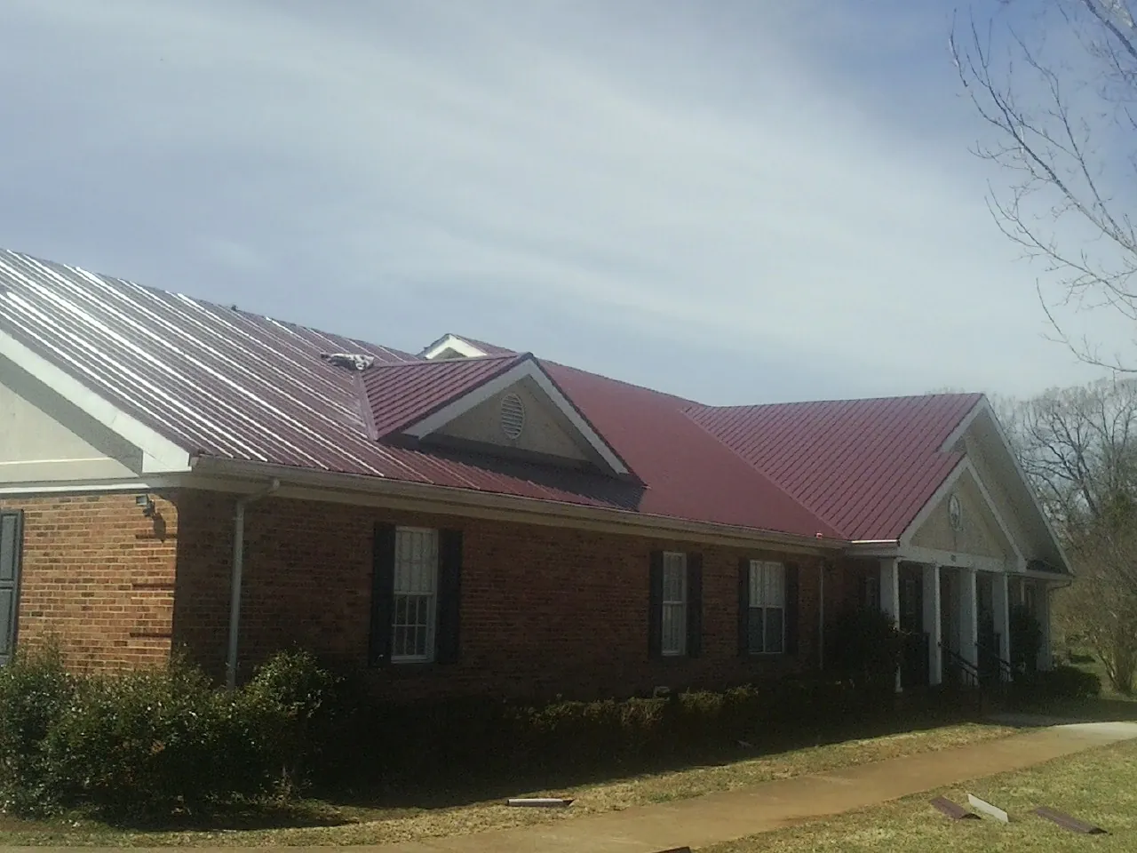 Red metal roof with gabled entries on a long brick building, from a Hail Damage Roof Repair job in Nodaway