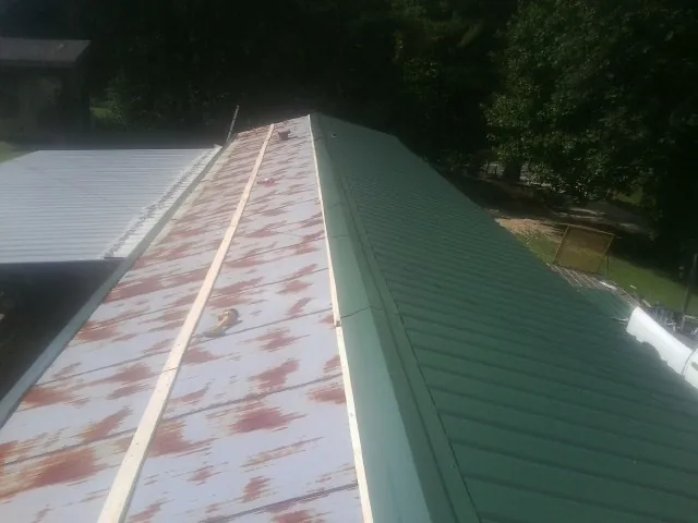 Old rusted panels beside newly installed green metal roofing — Wind Damage Roof Repair by Roofing Brothers in Nodaway