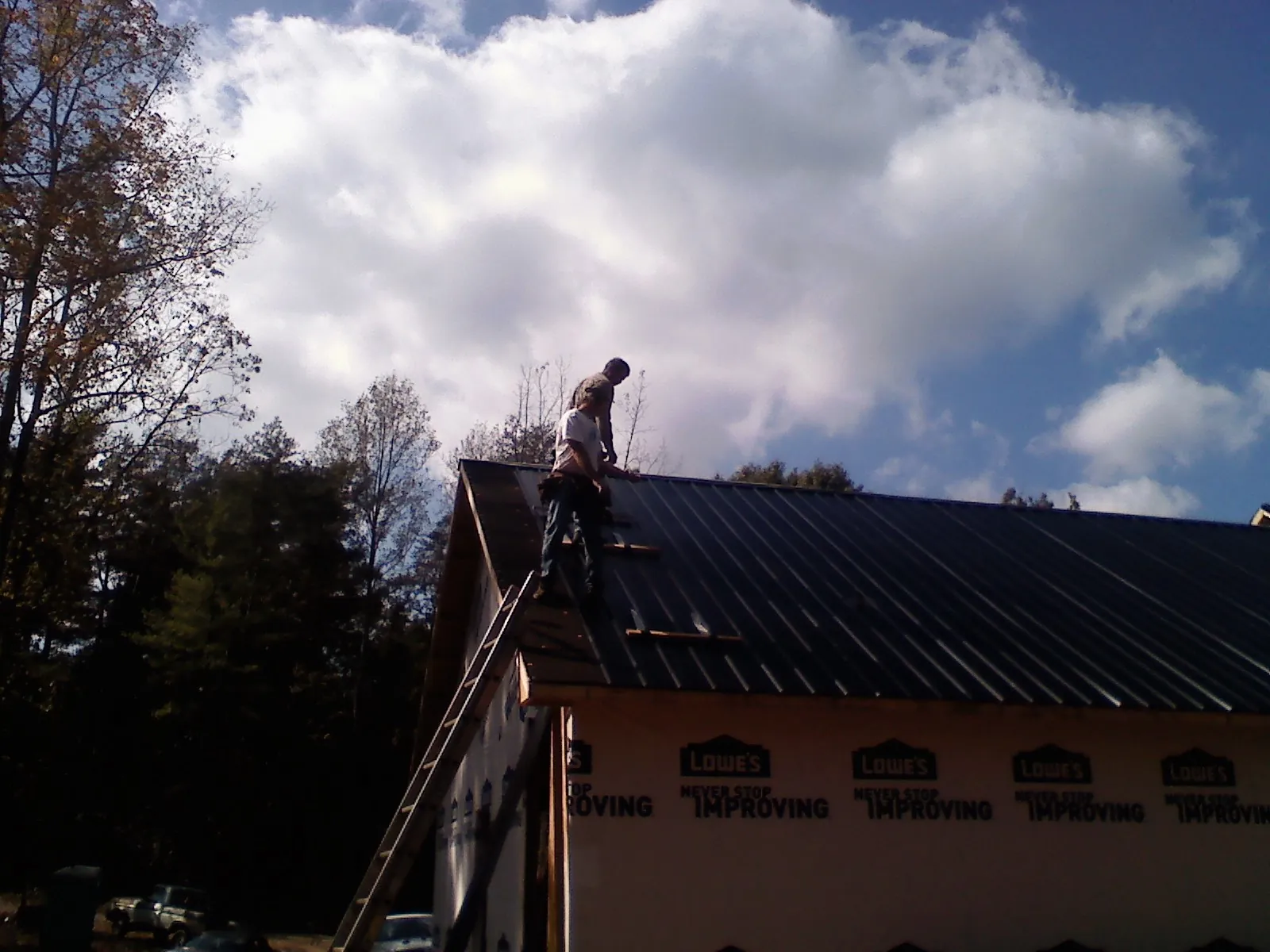 Roofer fastening dark metal panels high against a cloudy sky, from a Roof Inspection job in Nodaway