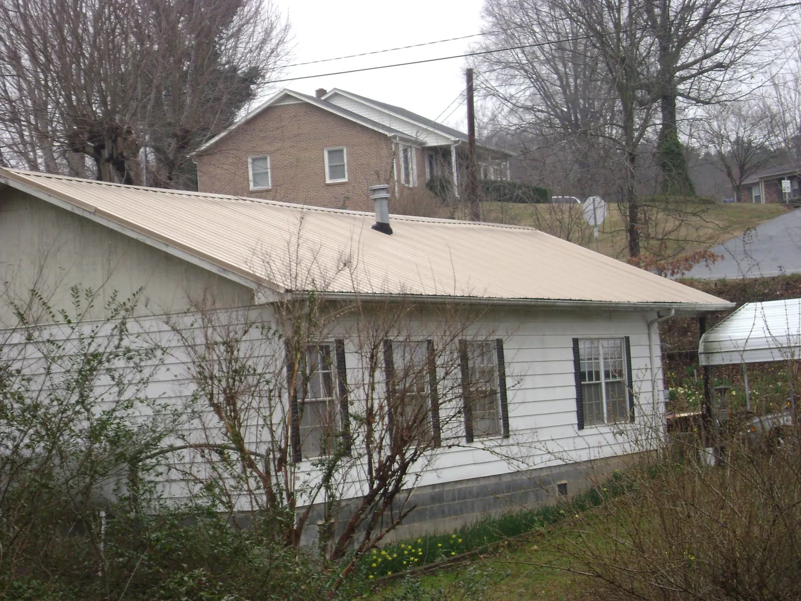 Tan metal roof on a white sided house set into a hillside — Commercial Roofing by Roofing Brothers in Nodaway