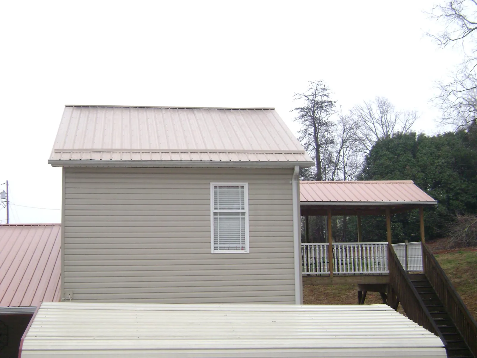 Tan metal roofs on a two story addition and attached porch, from a Roof Replacement job in Nodaway